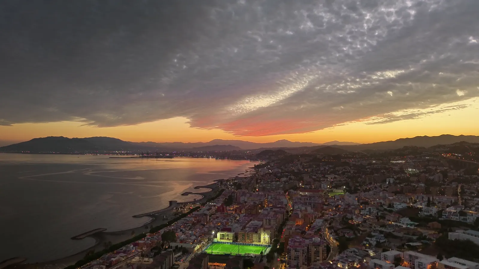 Vista aérea de la costa de Málaga al atardecer con la ciudad iluminada y las montañas al fondo